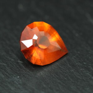 Macrofoto van een oranje spessartietgranaat van 5,3 karaat met een Aqua Drop-slijping op een zwarte leisteen.