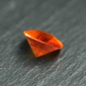 Macrofoto van een oranje spessartietgranaat van 5,3 karaat met een Aqua Drop-slijping op een zwarte leisteen.