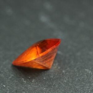 Macrofoto van een oranje spessartietgranaat van 5,3 karaat met een Aqua Drop-slijping op een zwarte leisteen.