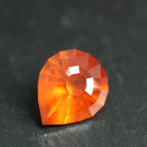 Macrofoto van een oranje spessartietgranaat van 5,3 karaat met een Aqua Drop-slijping op een zwarte leisteen.