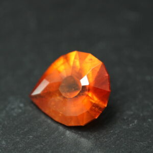 Macrofoto van een oranje spessartietgranaat van 5,3 karaat met een Aqua Drop-slijping op een zwarte leisteen.